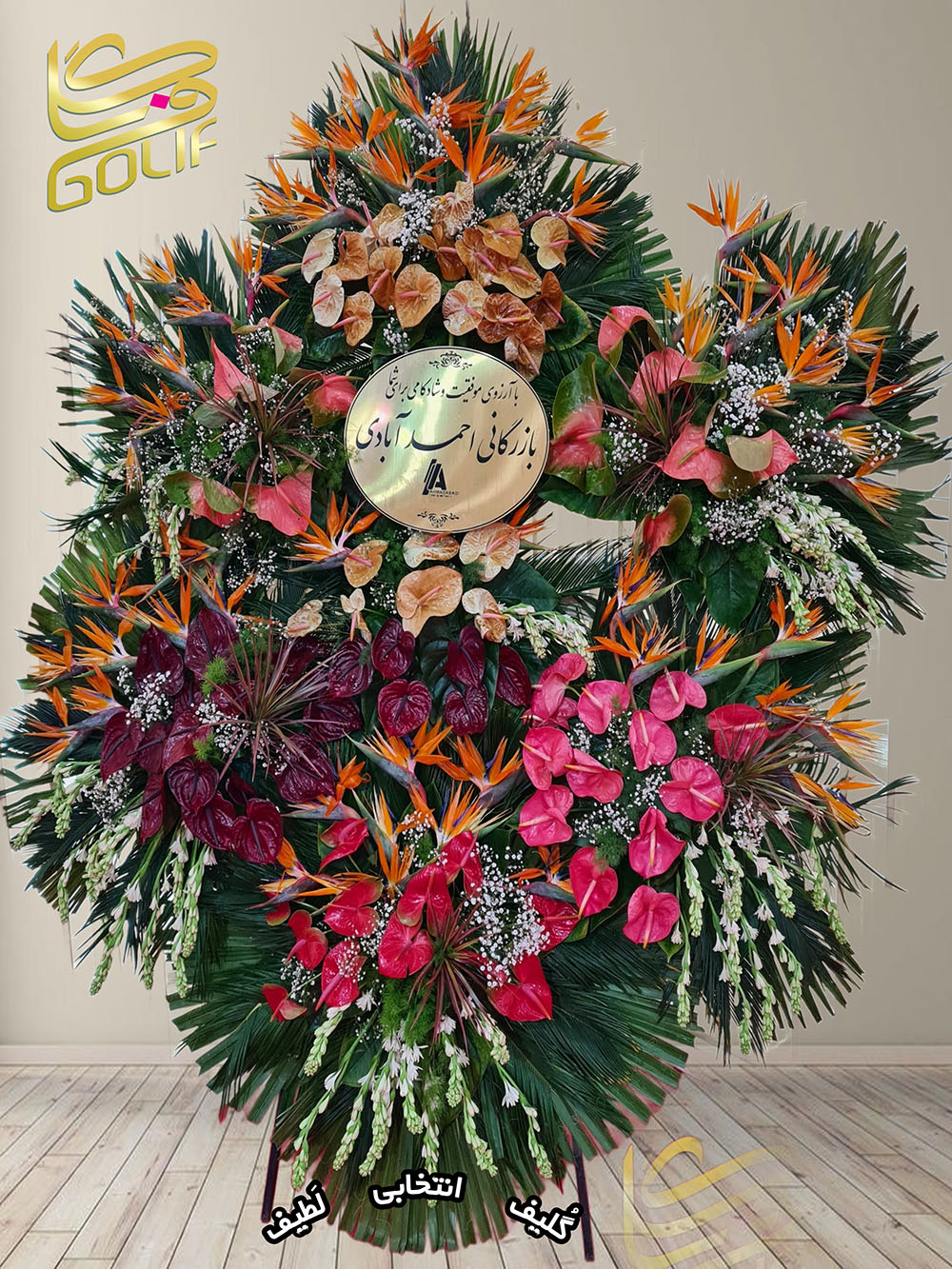 تاج گل تبریک هفت طبقه (آنتوریوم، مرغ بهشتی، ژربرا) گل‌های اصلی و غالب این تاج گل شامل موارد زیر هستند: آنتوریوم قرمز و صورتی: این گل‌ها در بخش پایینی طراحی خودنمایی می‌کنند و زیبایی ویژه‌ای به این طبقه داده‌اند. پرنده بهشتی نارنجی و آبی: در طبقه بالایی تاج گل برجسته‌ترین نقش را دارند و جذابیت بصری فوق‌العاده‌ای ایجاد کرده‌اند. ژربرای سفید: در طبقه میانی حضور دارند و جلوه‌ای لطیف و آرامش‌بخش ایجاد کرده‌اند. این گل‌ها در کنار برگ‌های سبز و طراحی چندطبقه‌ای، شکوه و هماهنگی خاصی به این تاج گل بخشیده‌اند. تاج گل افتتاحیه، تاج گل نمایشگاهی، تاج گل عقد و عروسی سفارش آنلاین تاج گل سفارش آنلاین گل عکاسی شده توسط گل‌فروشی آنلاین گلیف